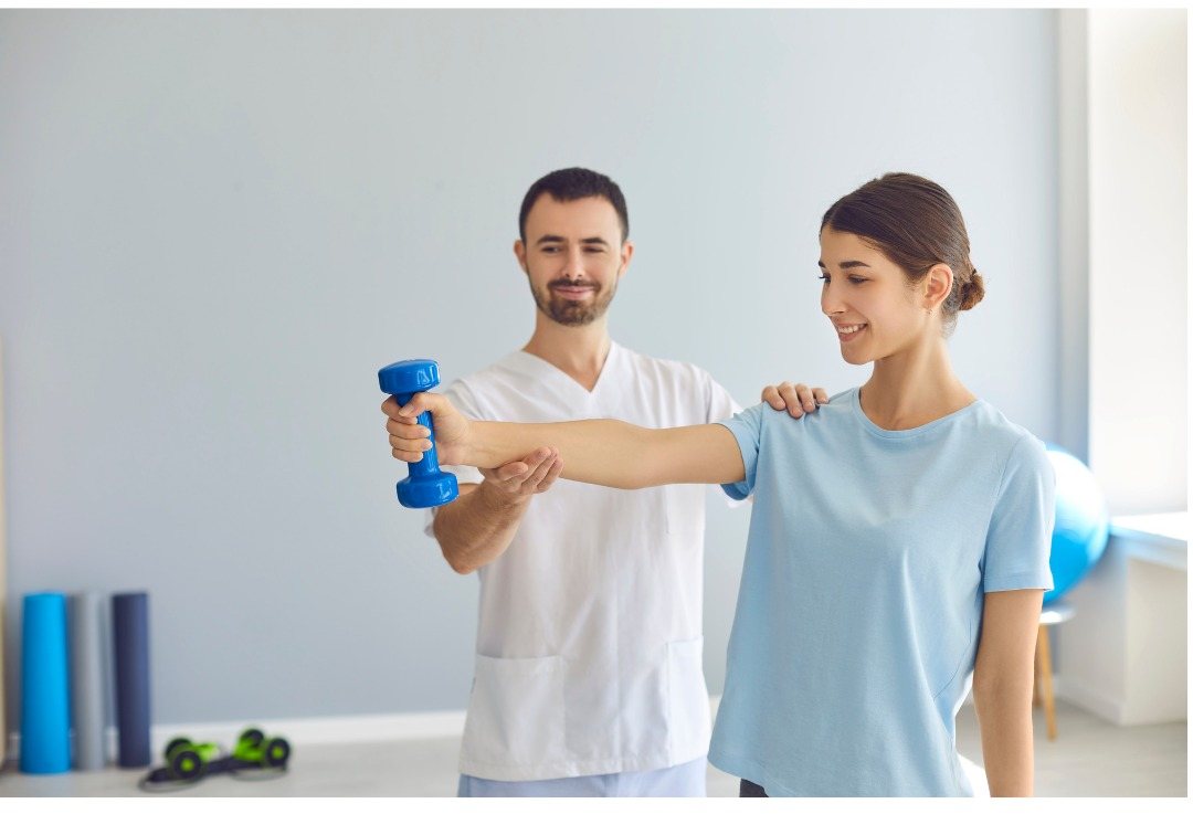Physiotherapist supervising shoulder strengthening with a dumbbell at RMC Mangalore